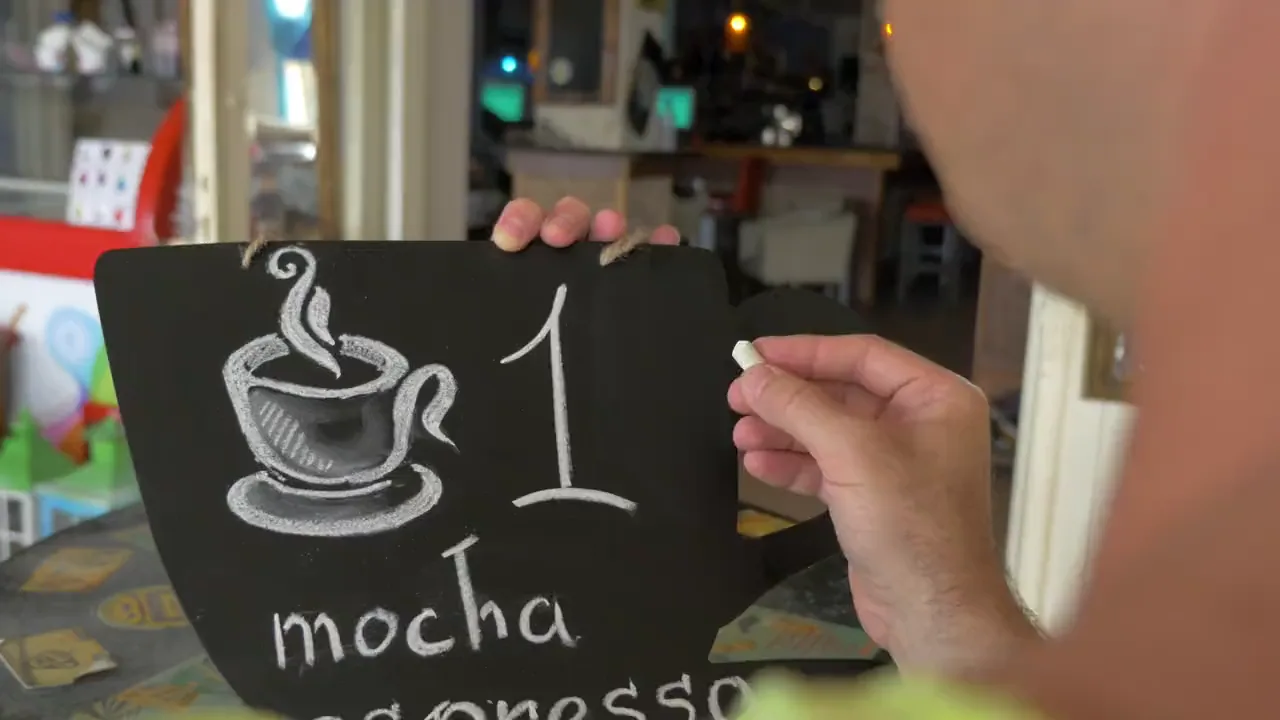 Una mano che scrive a gesso i prezzi sulla lavagna di un locale